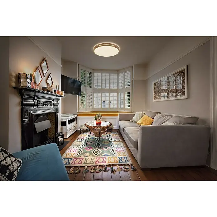 Osram Orbis LED-Deckenleuchte rund Woodburry - 16 W, Ø x H: 30 x 6,5 cm, Holzdekor, Warmweiß - Ein gemütliches Wohnzimmer mit einem stilvollen Teppich, einer bequemen Couch und einem dekorativen Kamin, beleuchtet durch eine moderne Deckenleuchte.