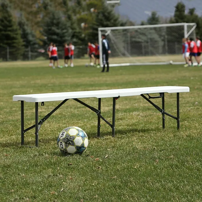 Lifetime Gartenbank - B x T x H: 183 x 29 x 42 cm, Weiß/Schwarz, Klappbar - Weisse Bank mit schwarzem Gestell und ein Fußball auf einem grünen Rasen. Im Hintergrund sieht man eine Fußballmannschaft beim Training.