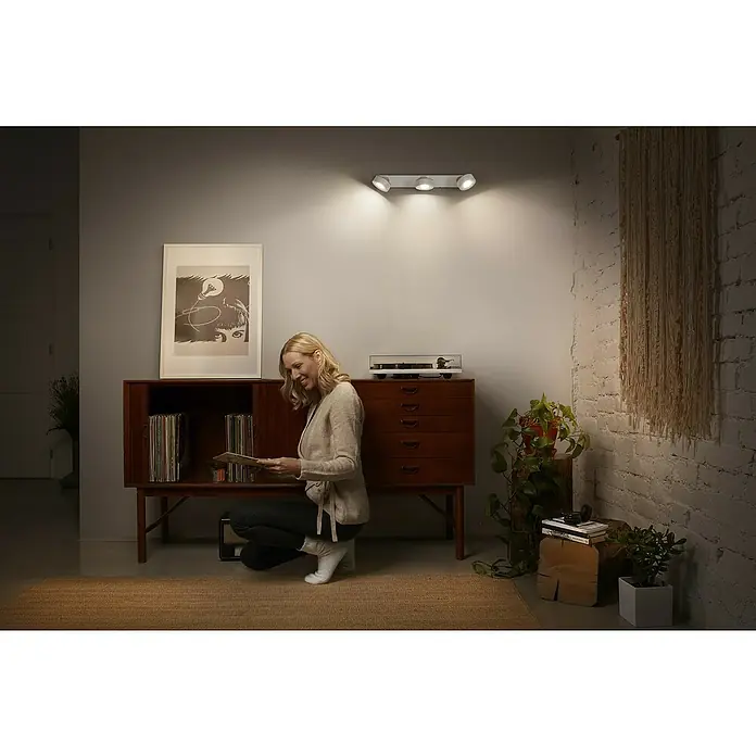 Ledvance LED-Wand- & Deckenstrahler Spot Pluto - 14,4 W, L x B x H: 49,8 x 9 x 10,8 cm, Weiß, Warmweiß, 3 Stk. - Wandleuchte mit drei Strahlern, die ein warmes Licht spenden, während eine Frau Schallplatten durchstöbert.