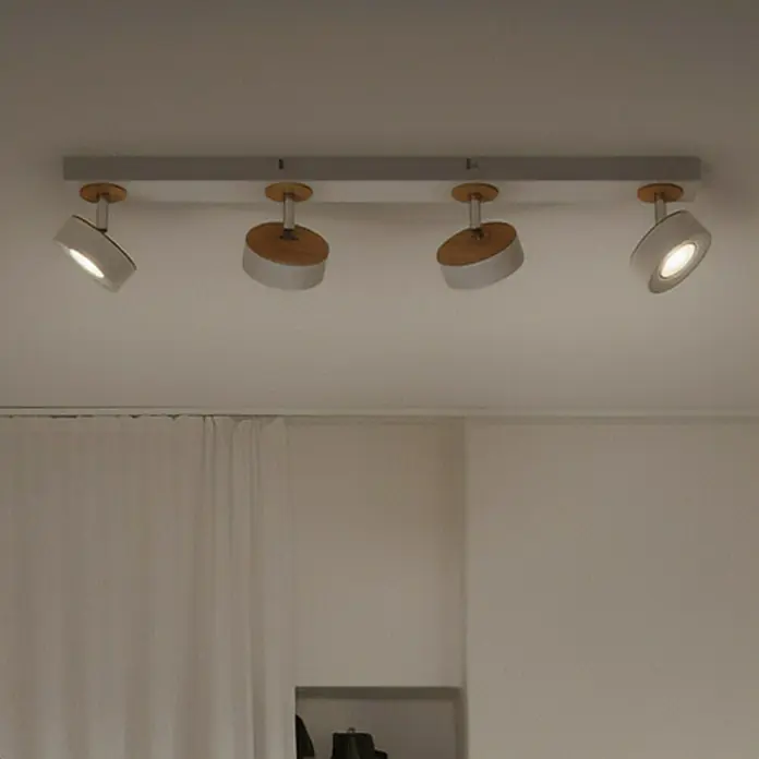 Ledvance LED-Wand- & Deckenstrahler Spot Pluto - 19,2 W, L x B x H: 69,8 x 9 x 10,8 cm, Weiß, Warmweiß, 4 Stk. - Nahaufnahme einer modernen Deckenleuchte mit vier Strahlern, die ein warmes Licht abgeben. Das Design ist minimalistisch mit Holz- und Metallelementen.