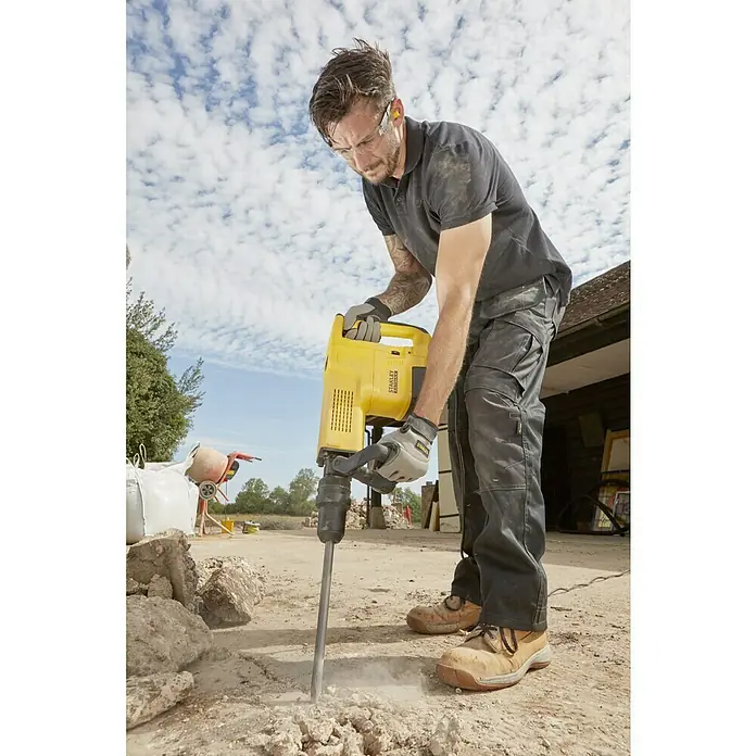 Stanley FatMax Martillo demoledor SFMEH230K-QS - 1.600 W, 15 J, Alojamiento SDS-MAX - El hombre usa un martillo de demolición Stanley amarillo para romper el suelo. Lleva equipo de protección, incluidas gafas y guantes.