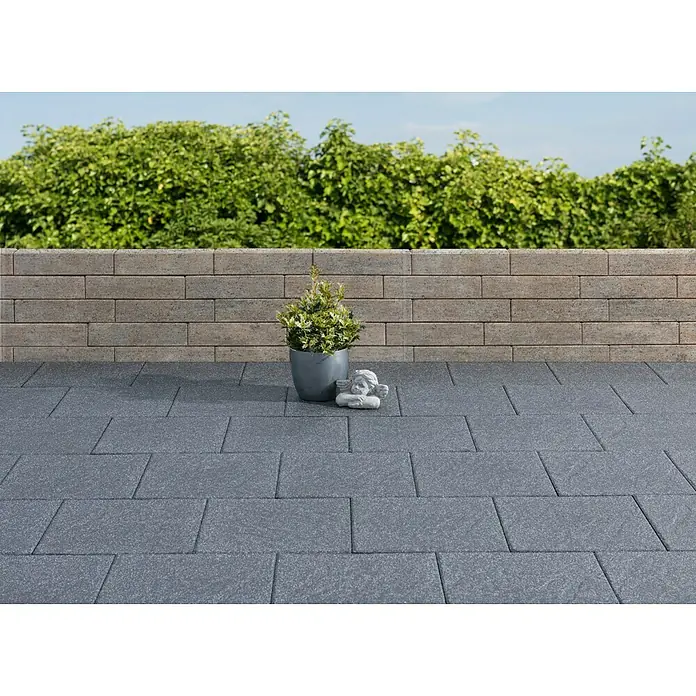 Diephaus Palisade / Mauerstein Laredo - 40 x 10 x 10 cm, Muschelkalk, Beton - Gartenbild mit Pflastersteinen in Anthrazit, einer kleinen Statue und einem Topf mit Grünpflanzen vor einer Steinmauer mit Bewuchs.
