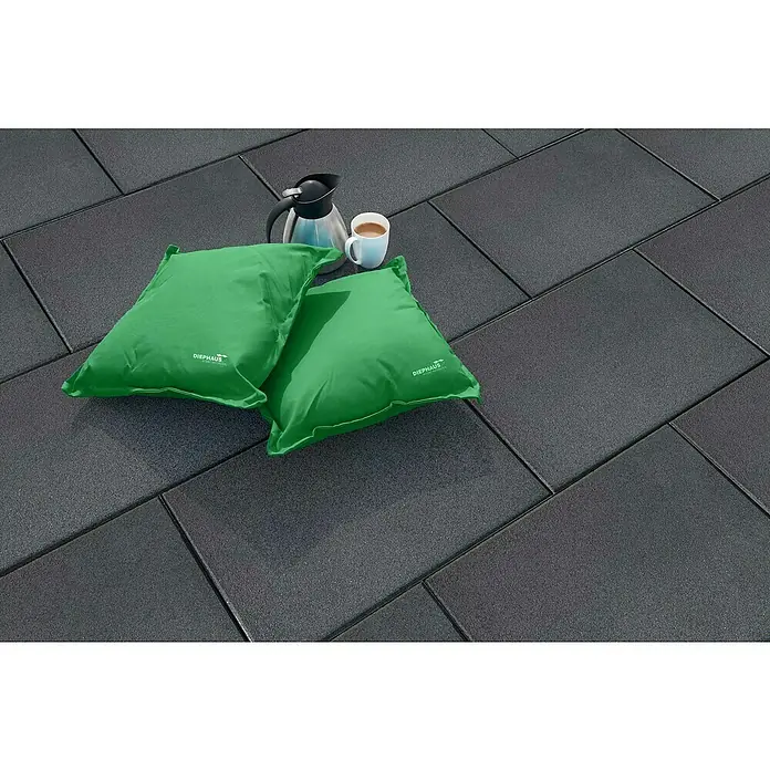 Diephaus Terrassenplatte Norfolg60 x 40 x 4 cm, Schwarz/Basalt, Beton - Ein Arrangement mit zwei grünen Kissen der Marke DIEPHAUS, einer Thermoskanne und einer Tasse auf einem grauen Steinboden.