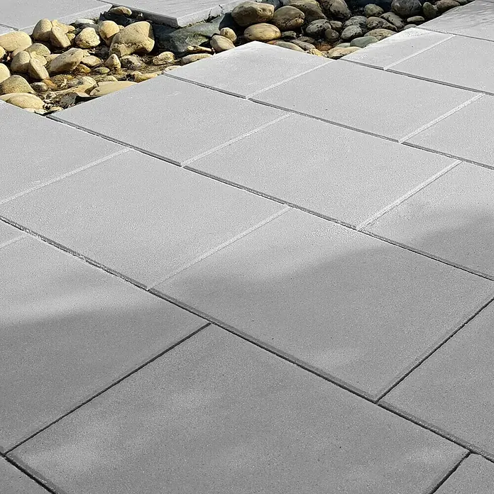 Diephaus Terrassenplatte Norfolg - 60 x 40 x 4 cm, Mittelgrau, Beton - Nahaufnahme von grauen Pflastersteinen neben einem dekorativen Bachbett mit runden Steinen, die eine moderne Gartengestaltung zeigen.