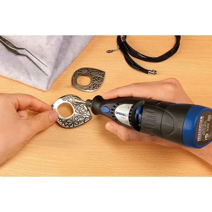 Dremel Messingbürste 537 - Kopfform: Pinselkopf, Arbeitsdurchmesser: 3,2 mm, 3 Stk. - Nahaufnahme eines Dremel-Rotationswerkzeugs beim Polieren von Schmuck, der auf einem Holztisch liegt. Ideal für detaillierte Handwerksarbeiten.