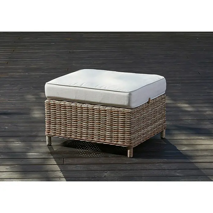 Taburete reposapiés Gotland - L x An x Al: 61 x 51 x 40 cm, Arena - Primer plano de un otomano cuadrado de ratán con un cojín de color crema en un patio exterior de madera.