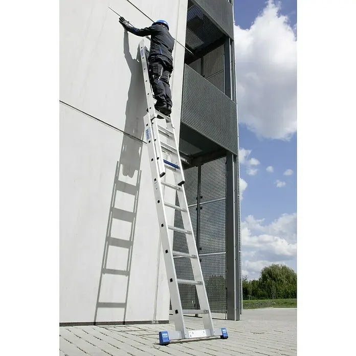 Krause Stabilo Schiebeleiter +S - Anzahl Tritte: 18 Stk., Arbeitshöhe: 5,15 m, Aluminium - Eine Teleskop-Schiebeleiter von KRAUSE im Einsatz, ein Arbeiter steht darauf und inspiziert die Wand. Die Leiter ist stabil und sicher.