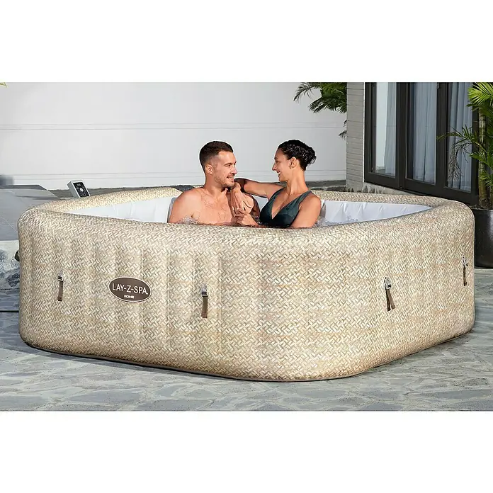 Bestway Lay-Z-Spa Mobil-Whirlpool Rome Air Jet - L x B x H: 180 x 180 x 71 cm, Beige, 840 l - Ein Lay-Z-Spa Whirlpool für zwei Personen mit beigem Rautenmuster auf einer Terrasse, umgeben von Pflanzen und Fenstern.