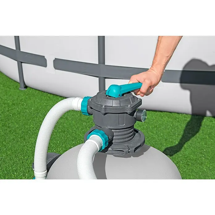 Bestway Sandfilteranlage - Filterleistung: 7.570 l/h, Passend für Poolgröße: 60.500 l - Detailaufnahme einer Person, die den blauen Hebel eines grauen Poolfilters betätigt, mit einem Pool im Hintergrund.