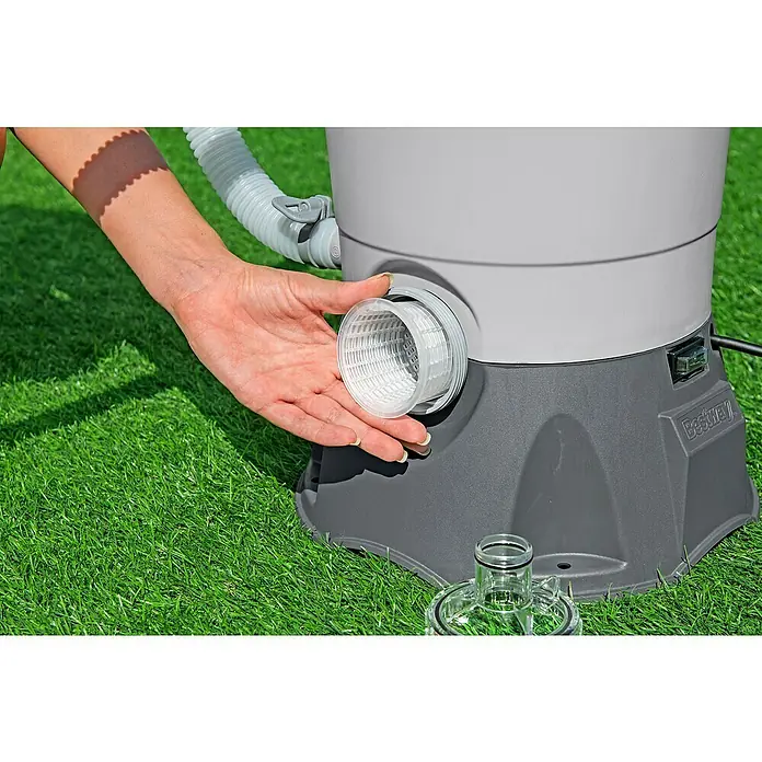 Bestway Sandfilteranlage - Filterleistung: 2.082 l/h, Passend für Poolgröße: 16.600 l - Aufnahme einer Person, die den Filter einer Bestway-Poolpumpe installiert. Das Gerät steht auf grünem Gras und ist mit Schläuchen verbunden.