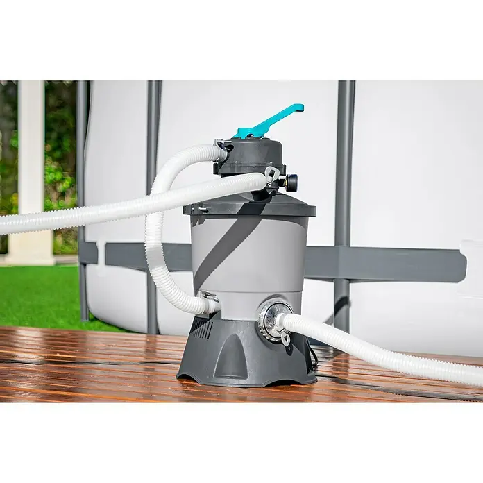 Bestway Sandfilteranlage - Filterleistung: 2.082 l/h, Passend für Poolgröße: 16.600 l - Eine graue Poolfilterpumpe mit blauen Akzenten und weißen Schläuchen steht auf einem Holztisch. Der Filter ist an einen Pool angeschlossen.