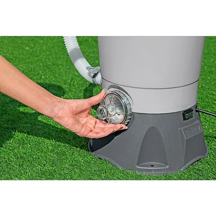 Bestway Sandfilteranlage - Filterleistung: 2.082 l/h, Passend für Poolgröße: 16.600 l - Nahaufnahme einer Hand, die den transparenten Filter einer Bestway-Poolpumpe auf grünem Rasen berührt.
