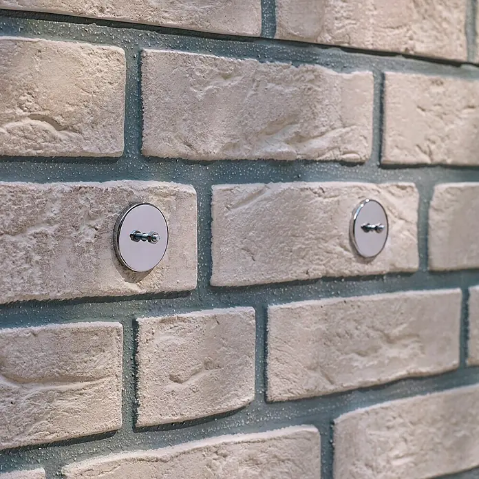 Tesa Tornillo adhesivo - Redonda, Carga soportada: 10 kg, 2 ud. - Primer plano de una pared de ladrillo con dos soportes de pared redondos y brillantes integrados sutilmente en la mampostería.