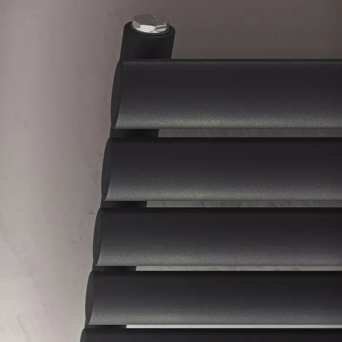 Ximax Raumheizkörper Fortuna Horizontal - B x H: 1.200 x 584 mm, Wärmeleistung bei Vorlauftemperatur von 75 °C (D: 50): 758 W, Anthrazit - Nahaufnahme eines modernen, schwarzen Heizkörpers mit horizontalen Lamellen, der an einer hellen Wand befestigt ist.