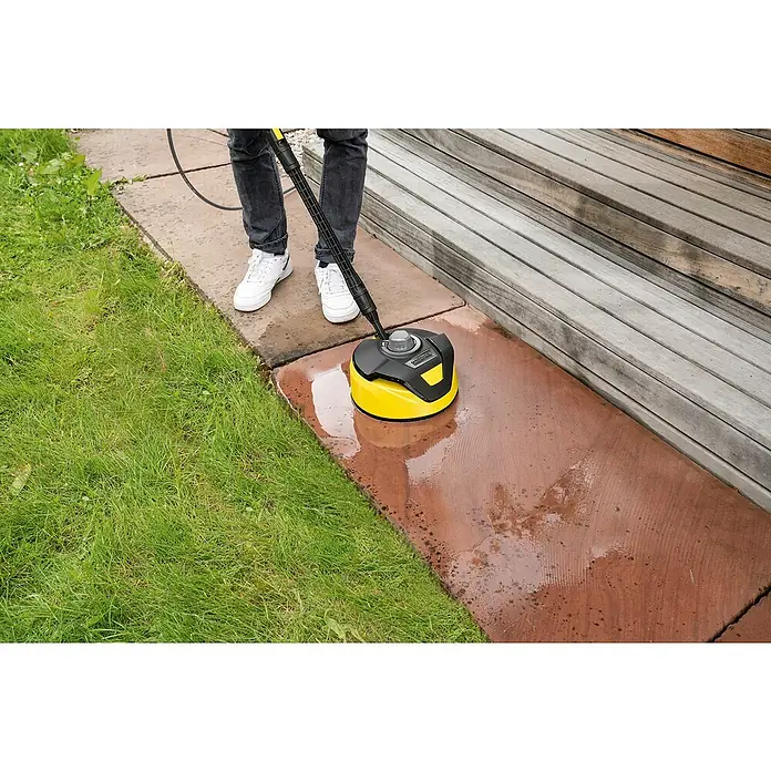 Kärcher Hochdruckreiniger K 4 Pure Flex Home - 1.800 W, Max. Druck: 130 bar, Fördermenge: 420 l/h - Gelber Kärcher Flächenreiniger im Einsatz auf einer Steinplatte, bedient von einer Person in Jeans und weißen Schuhen.