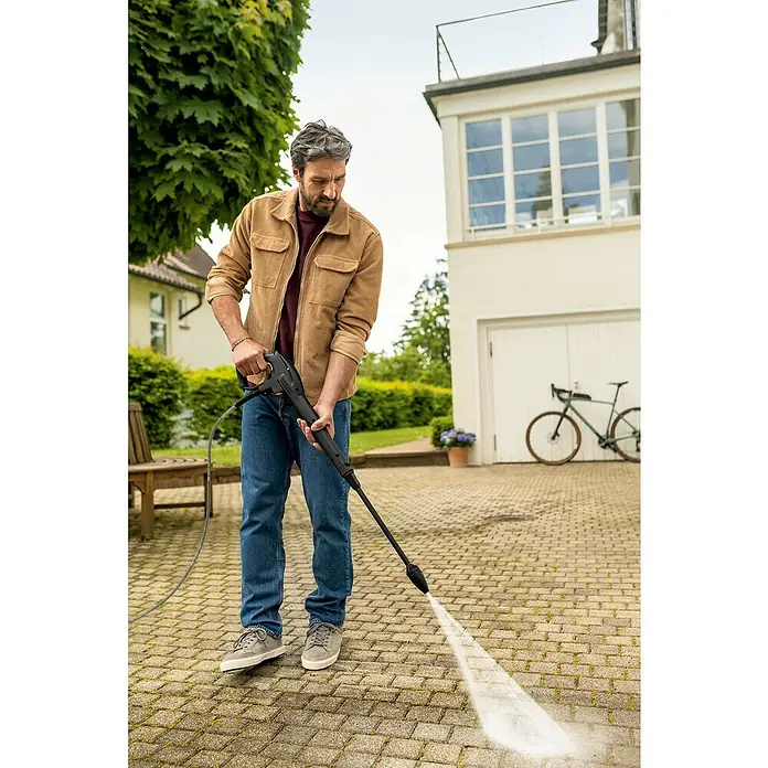 Kärcher Hochdruckreiniger K 4 Pure Flex Home - 1.800 W, Max. Druck: 130 bar, Fördermenge: 420 l/h - Ein Mann benutzt einen Kärcher Hochdruckreiniger, um eine gepflasterte Fläche im Freien zu reinigen. Der Reiniger entfernt Schmutz und Grünbelag.