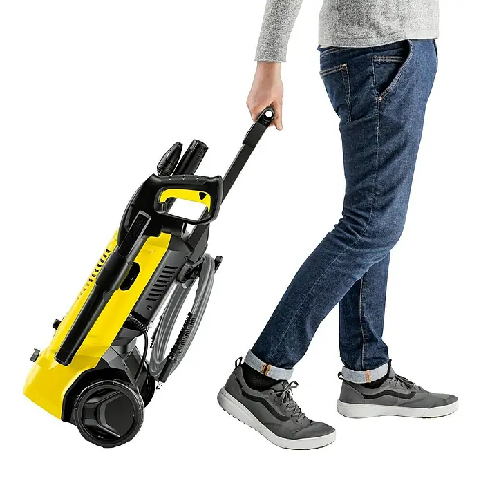 Kärcher Hochdruckreiniger K 4 Pure Flex Home - 1.800 W, Max. Druck: 130 bar, Fördermenge: 420 l/h - Eine Person zieht einen gelben Kärcher Hochdruckreiniger auf einem schwarzen Hintergrund.