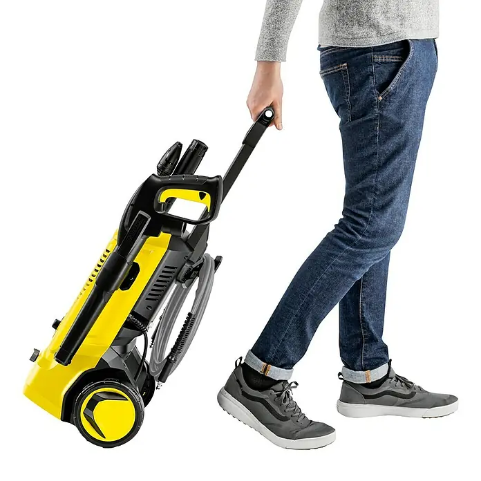 Kärcher Hochdruckreiniger K 5 Pure Flex Home - 2.100 W, Max. Druck: 145 bar, Fördermenge: 500 l/h - Ein Mann zieht einen gelben Kärcher Hochdruckreiniger hinter sich her. Der Reiniger ist kompakt und leicht zu transportieren.