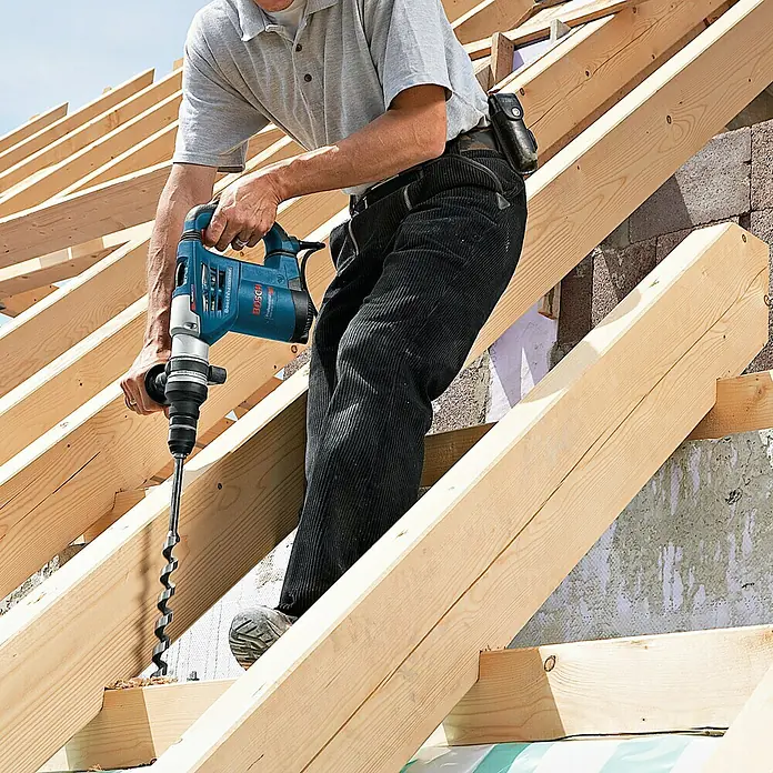 Bosch Professional Kombihammer GBH 4-32 DFR - 900 W, 4,2 J, SDS-Plus-Aufnahme - Ein Bauarbeiter bohrt mit einer blauen Bosch-Bohrmaschine Löcher in Holzbalken auf einer Baustelle.