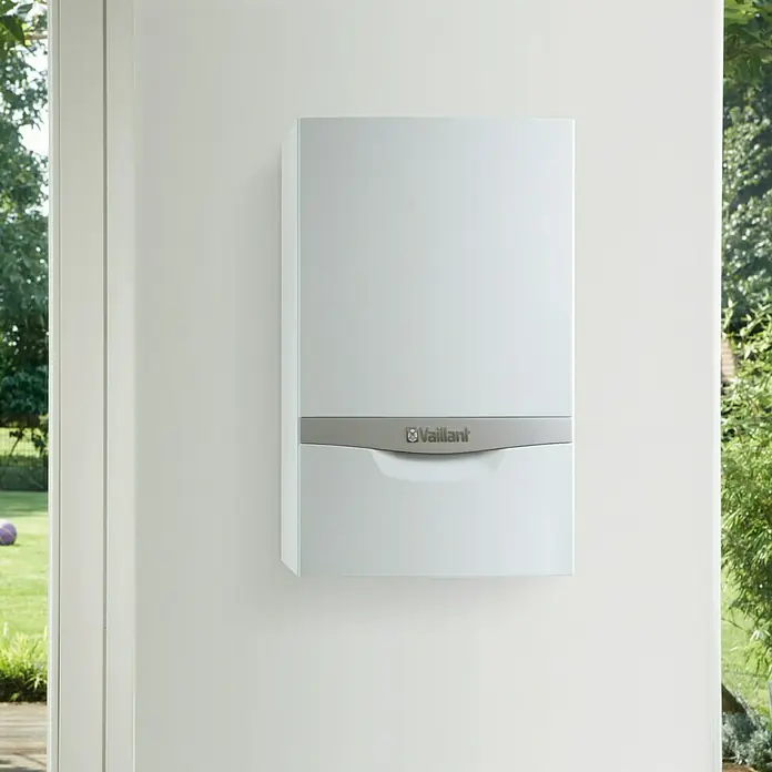 Vaillant Caldera EcoTEC Plus VMW 246 N - 24 kW, 10 l, Display multifunción - Unidad de calefacción Vaillant montada en la pared, rodeada de un fondo brillante y naturaleza. El aparato tiene un diseño limpio y moderno.