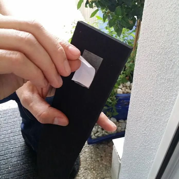Öko-Tec Dichtungszulage - XL, Selbstklebend, Kürzbar - Eine Person entfernt die Schutzfolie von einem schwarzen Dichtungsstreifen mit Klebefläche, um ihn anzubringen.