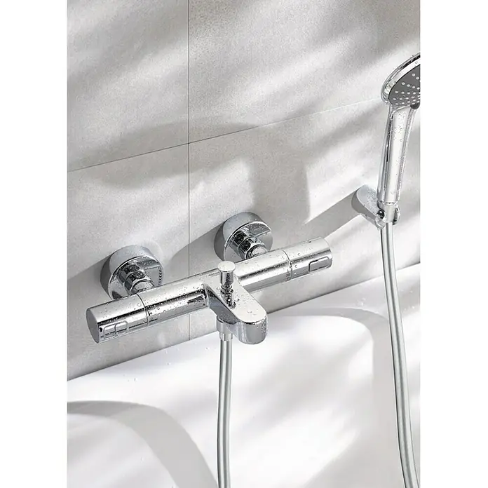 Grohe Thermostatarmatur Precision Joy - Breite: 29,9 cm, Chrom, Glänzend - Nahaufnahme einer glänzenden, verchromten Badewannenarmatur mit Brause an einer weißen Wand.