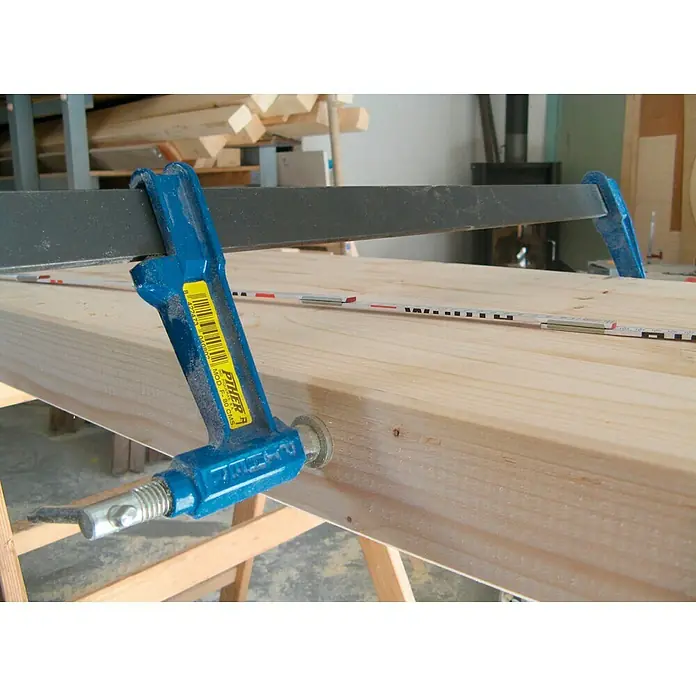 Piher Sargento F-40 - Anchura de sujeción: 400 mm, Fuerza de tensión: 9.000 N, Apertura máxima: 120 mm - Primer plano de una mordaza de barra azul PTHER que asegura una tabla de madera en un banco de trabajo, ideal para carpintería.