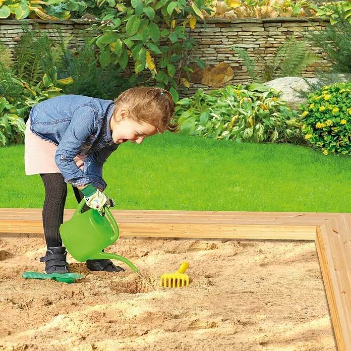 Gardol Kinder-Gartenhandschuhe Tiere - Handschuhgröße: 5, Gelb - Mädchen gießt Sand mit grüner Gießkanne, Spielzeugrechen daneben. Sandkasten mit Holzrahmen im Garten.