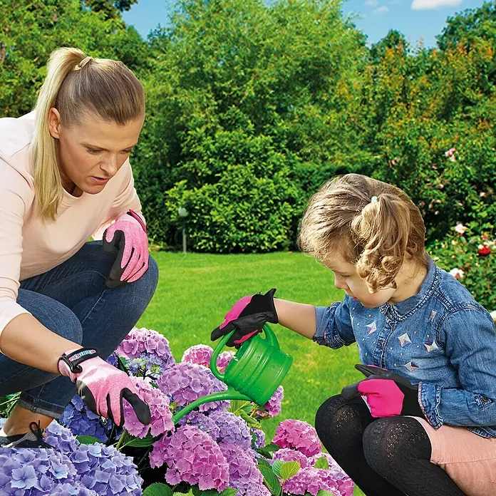 Gardol Kinder-Gartenhandschuhe5, Pink - Eine Frau und ein Kind gießen mit Gartenhandschuhen und einer grünen Gießkanne Blumen im Garten.