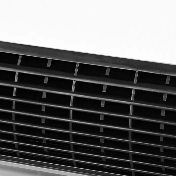 Voltomat HEATING Heizlüfter - 1.000 W - 2.000 W, Weiß, 29,5 x 19 x 31,6 cm, IP22 - Nahaufnahme eines schwarzen Lüftungsgitters. Das Gitter hat horizontale Lamellen und vertikale Stützen, die ein regelmäßiges Muster bilden.