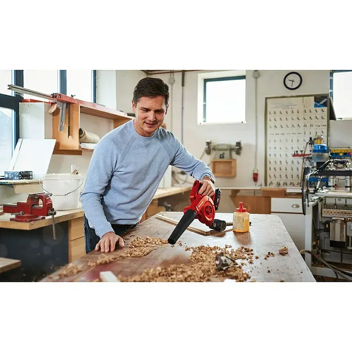 Einhell Power X-Change 18V Akku-Gebläse TE-CB 18/180 Li-Solo - 18 V, Ohne Akku, Blasgeschwindigkeit: 130 km/h - Mann reinigt Werkbank mit einem roten Einhell Akku-Laubbläser. Perfekt für die schnelle und mühelose Reinigung von Werkstätten.