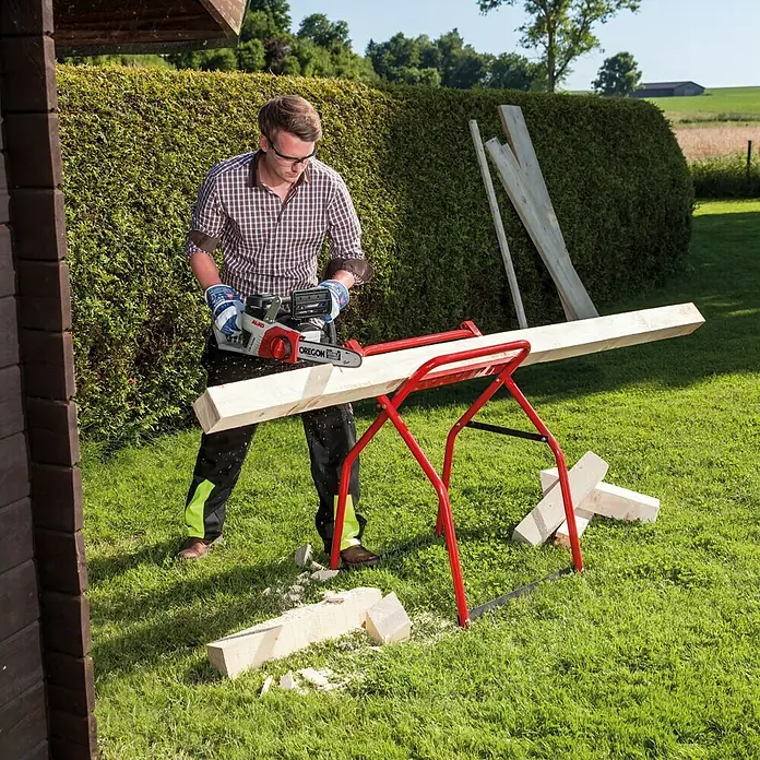 AL-KO 36V Akku-Kettensäge CS 4030 - 36 V, Li-Ionen, Ohne Akku, Schwertlänge: 30 cm - Ein Mann sägt mit einer Oregon-Kettensäge ein Holzbrett auf einem roten Sägebock im Garten.