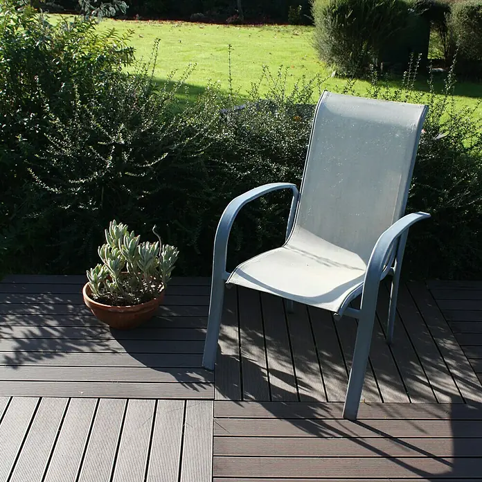 Dioco Loseta de WPC - Chocolate, An x L: 90 x 90 cm, 1 ud. - Primer plano de una cómoda silla de patio en una terraza, con una planta suculenta en maceta y un exuberante entorno verde.