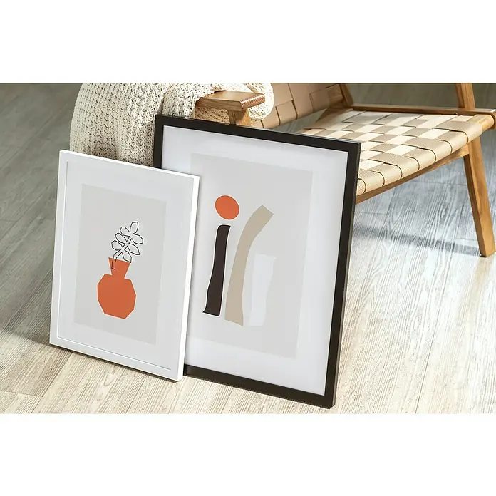Accent Holzrahmen Wood - 30 x 40 cm, Weiß - Zwei gerahmte Kunstwerke, eines mit einem orangefarbenen Topf und Pflanzen, das andere mit abstrakten Formen, stehen auf einem Holzboden, der eine moderne Ästhetik vermittelt.