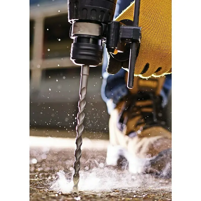 DeWalt Broca para hormigón y mampostería DT9514-QZ - 1 ud., Diámetro de la broca: 6 mm - Taladro en acción: Un primer plano de un taladro eléctrico perforando un agujero en una superficie, con polvo y partículas volando mientras trabaja.
