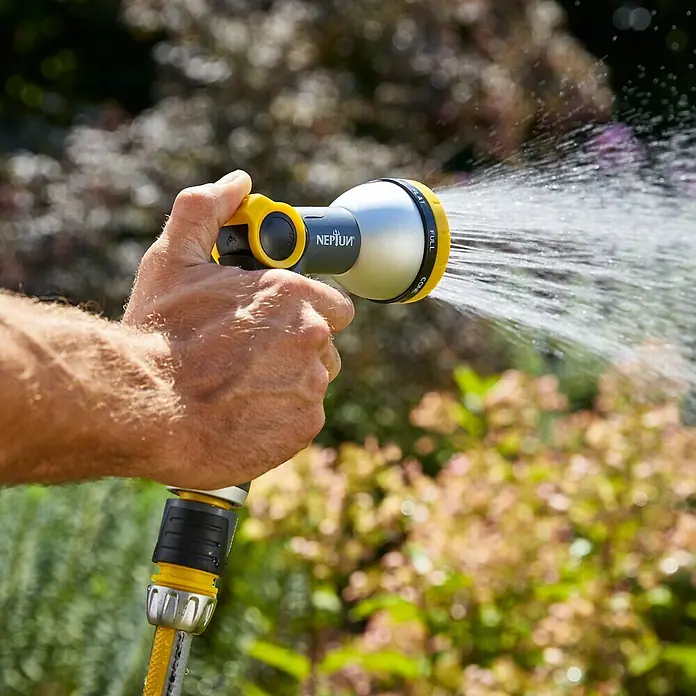 Neptun Profi Pistola multiuso - Aluminio/Plástico - Un hombre sujeta un rociador de jardín con detalles amarillos, rociando agua, sobre un fondo borroso.