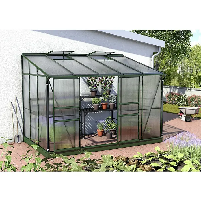 Vitavia Gewächshaus Osiris 6500 - Außenmaß inkl. Dachüberstand (B x T): 324,3 x 201 cm, 6 mm, Smaragd - Ein Gewächshaus mit Pflanzenregal, das mit verschiedenen Pflanzen und Blumen bestückt ist, steht auf einem gepflasterten Untergrund vor einer Hauswand.