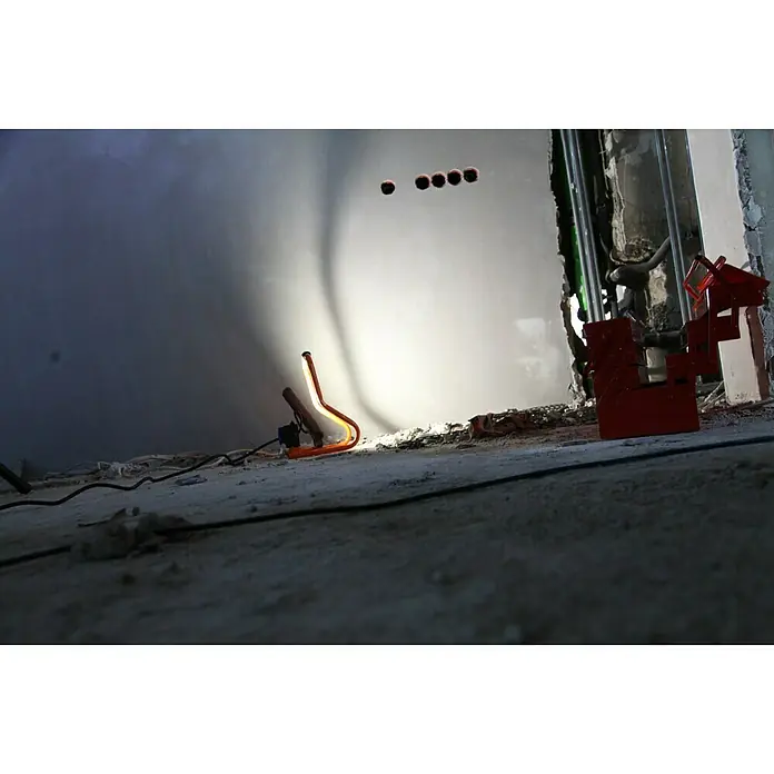 Ledvance LED-Strahler - 30 W, 2.700 lm, 4.000 K, L x B x H: 19 x 22 x 29 cm, IP44 - Nahaufnahme einer orangefarbenen Arbeitsleuchte, die eine Baustelle beleuchtet, mit freiliegenden Rohren und Werkzeugen im Hintergrund.