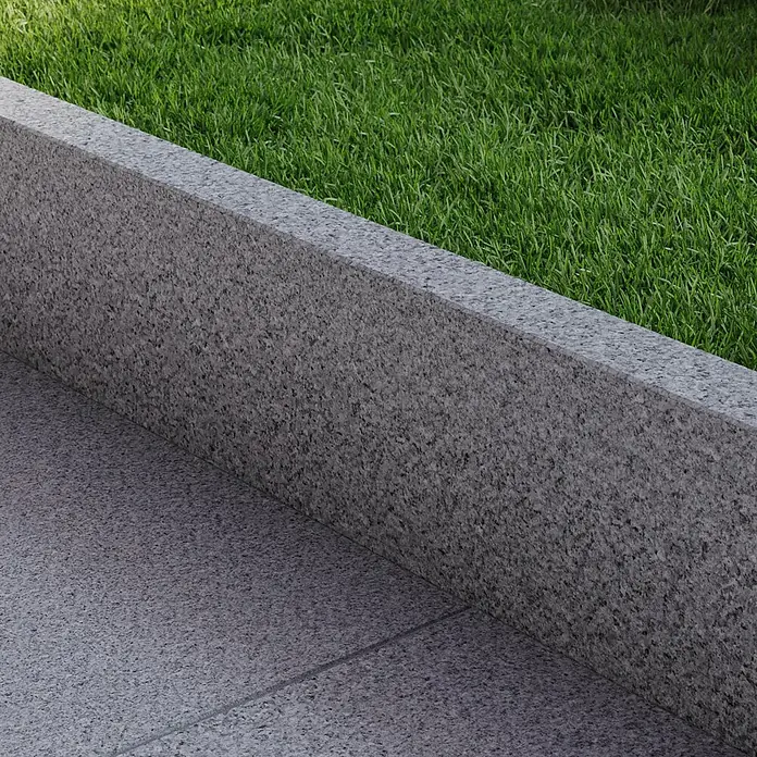 Rasenkante G 603 - 100 x 20 x 5 cm, Grau, Granit - Nahaufnahme eines grauen Granit-Bordsteins, der einen Rasen von einem gepflasterten Bereich trennt. Die Textur des Granits ist deutlich sichtbar.