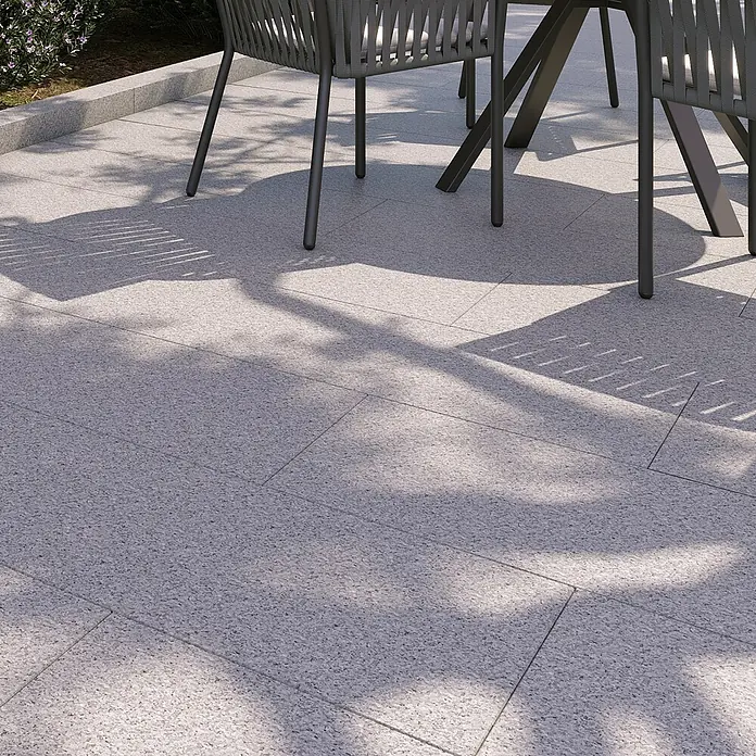 Terrassenplatte G 603 - 80 x 40 x 3 cm, Grau, Granit - Nahaufnahme eines Tisches und Stühle auf einem gepflasterten Bereich mit Schatten, die Textur und das Design der Gartenmöbel hervorheben.