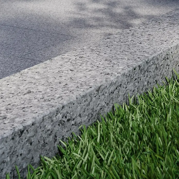Randstein G 603 - Grau, Granit - Nahaufnahme einer grauen Bordsteinkante aus Granit mit saftigem grünen Gras im Vordergrund, ideal für Straßen- und Gartendesign.
