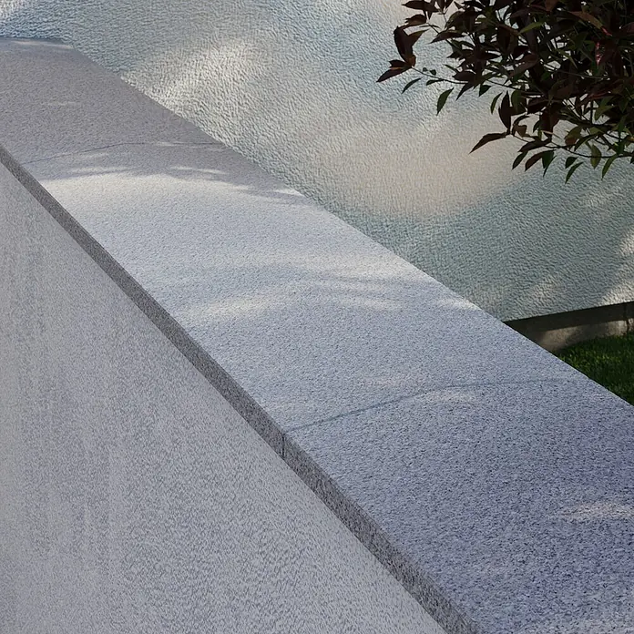 Mauerabdeckplatte G 603 - 100 x 29 x 2,5 cm, Grau, Granit - Nahaufnahme einer stilvollen grauen Steinmauer, die modernes Design und robuste Bauweise vereint. Perfekt für Außenbereiche.