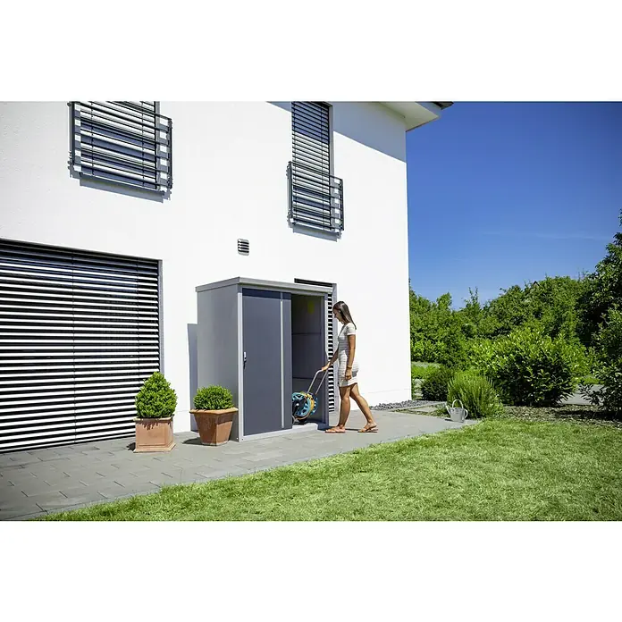Trimetals Geräteschrank Guardian D63 - Außenbreite inkl. Dachüberstand: 176 cm, Außentiefe inkl. Dachüberstand: 89 cm, Stahl, Lichtgrau - Frau holt Gartenschlauch aus Gerätehaus aus Metall. Praktische Gartenausrüstung für die Aufbewahrung von Gartengeräten.