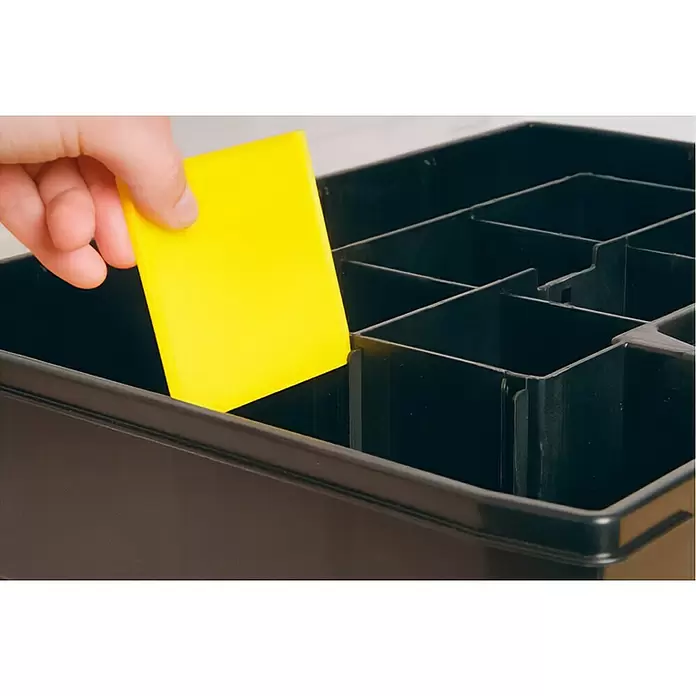 Stanley Estuche para piezas pequeñas Sortmaster - 3 pzs. - Organizador negro de plástico con compartimentos, una mano coloca un objeto amarillo.