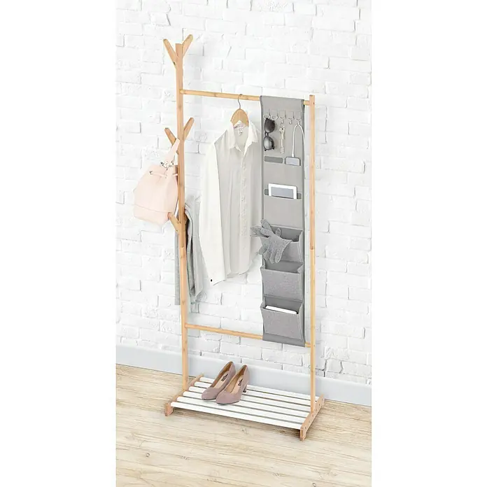 Perchero de pie con organizador colgante - L x An x Al: 38 x 65 x 167 cm, Número de ganchos: 6, Bambú/blanco - Un perchero de madera con ropa, zapatos y accesorios, sobre un fondo de pared de ladrillo blanco.
