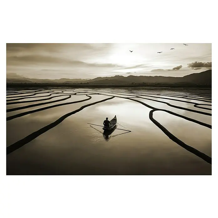 Cuadro Paisaje - Paisaje, An x Al: 140 x 90 cm, 1 pzs. - Un hombre rema en una estrecha barca a través de los campos de arroz inundados, reflejados en una luz suave, con pájaros en el cielo.