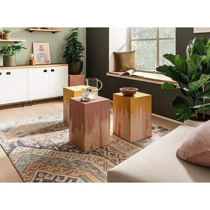 Noblewood Massivholzblock - Buche, 30 x 30 x 45 cm - Dieses Bild zeigt drei dekorative Holzhocker in verschiedenen Farben, die als Beistelltische im Wohnzimmer dienen.
