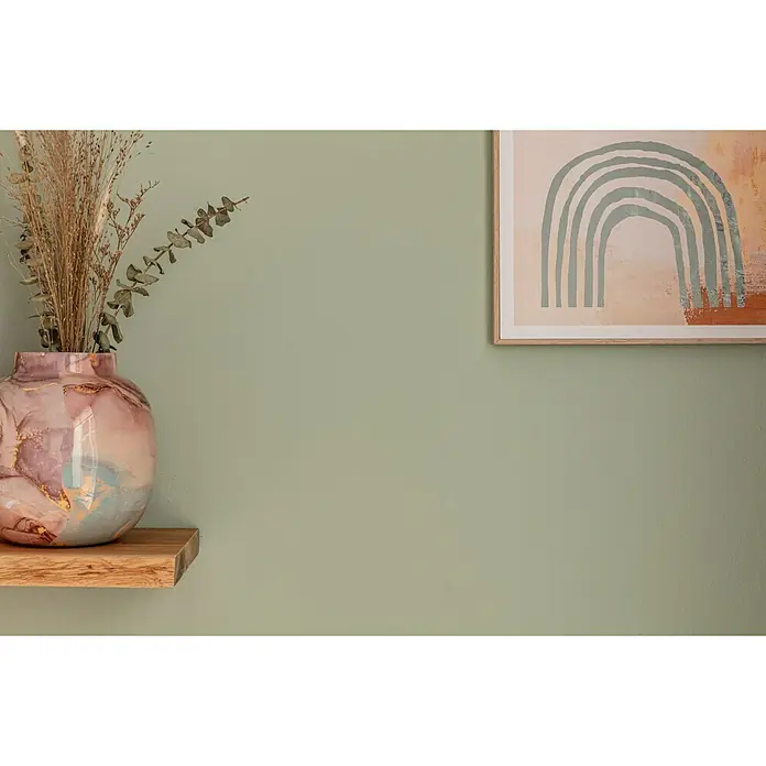 SCHÖNER WOHNEN-Farbe Naturell Wandfarbe Kreidefarbe - Frühlingserwachen - leichtes Olivgrün, Matt, 2,5 l, Konservierungsmittelfrei - Nahaufnahme einer dekorativen Vase mit Trockenblumen auf einem Holzregal und einem gerahmten Kunstdruck an einer grünen Wand.