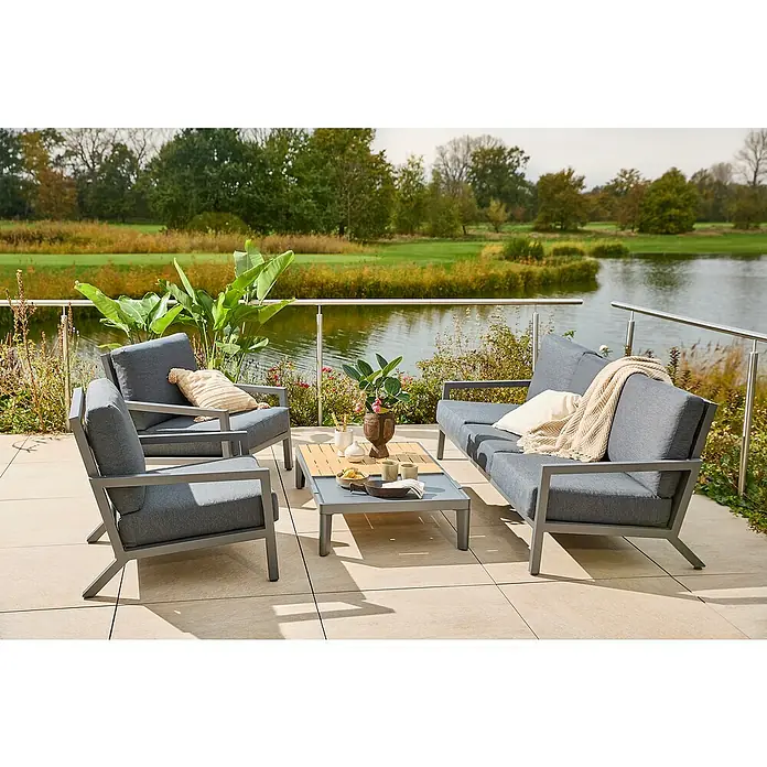 Sunfun Solo Garten-Couchtisch - L x B x H: 120 x 72 x 26 cm, Night-Grey - Moderne Gartensitzgruppe mit grauen Polstern und einem niedrigen Tisch auf einer Terrasse mit Blick auf einen See.