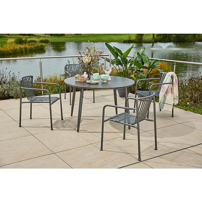 Sunfun Gartenmöbel-Set Solo/Sarah - 5 -tlg., Aluminium/Sintered Stone/Stahl, Night-Grey - Nahaufnahme eines grauen Gartentisches mit vier Stühlen auf einer Terrasse mit Blick auf einen ruhigen See. Das Set lädt zum Verweilen im Freien ein.